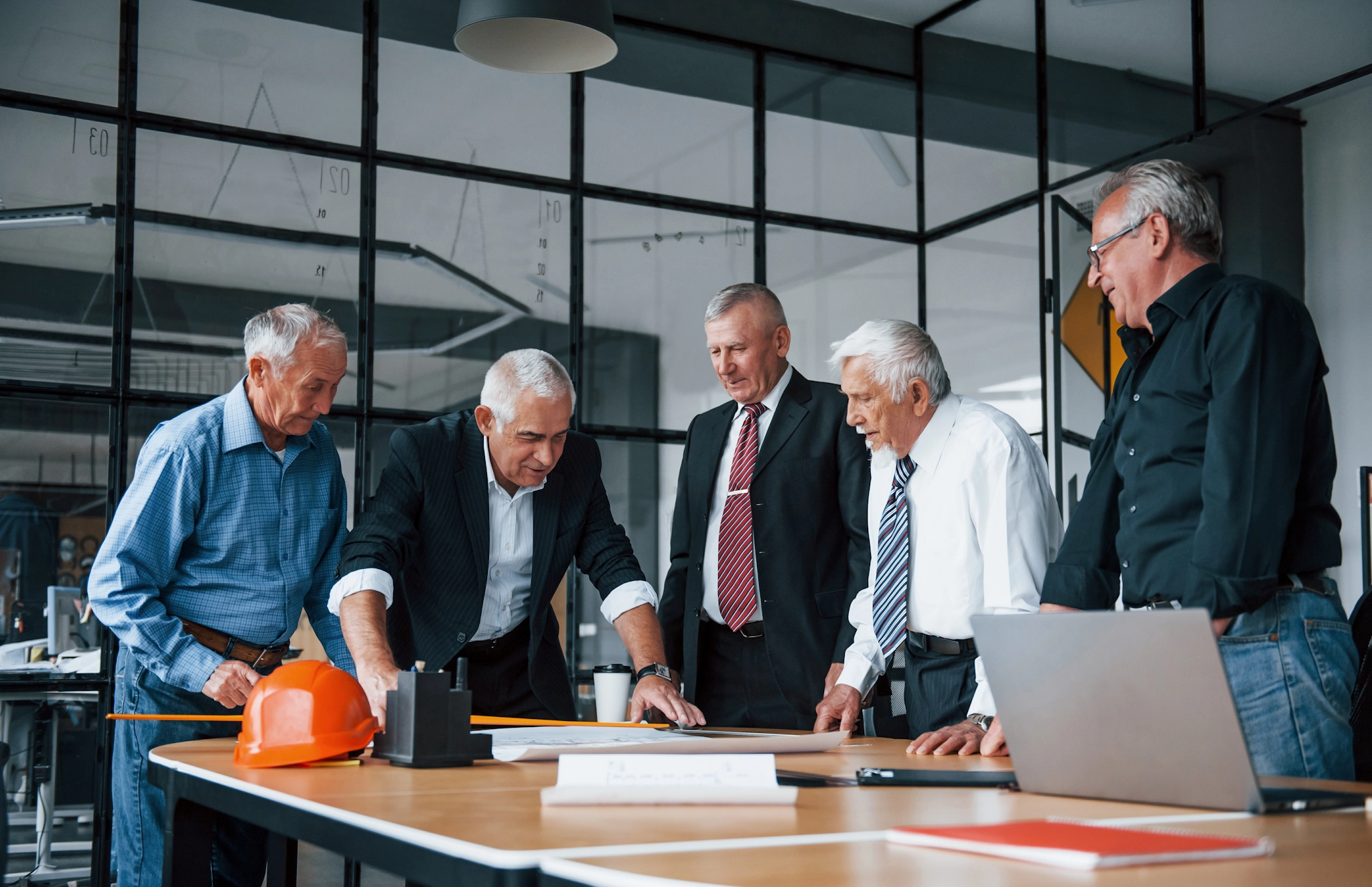 Aged team of elderly businessman architects works with plan in the office – representing collaboration and shared planning.